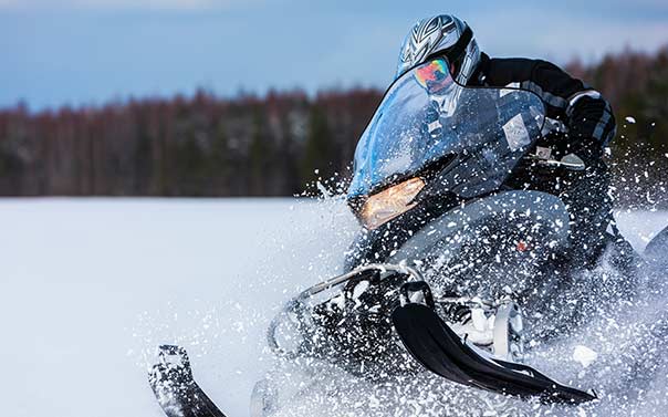 A person dressed in black riding a black and gray snowmobile through the snow 