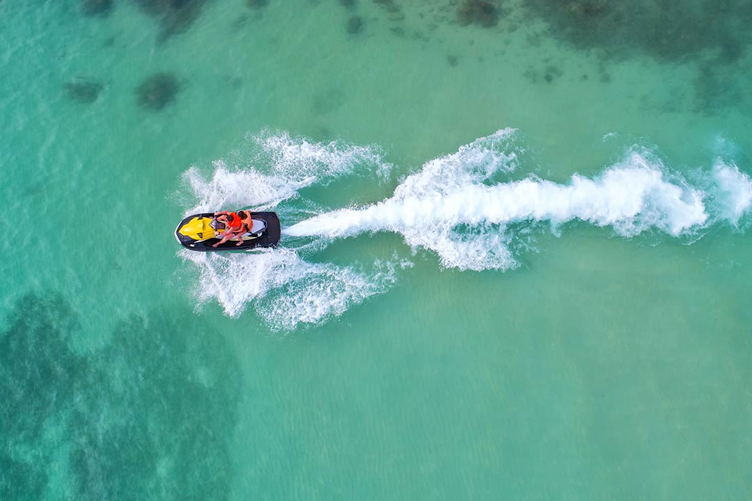 An aerial view of a couple on a watercraft in clear ocean water