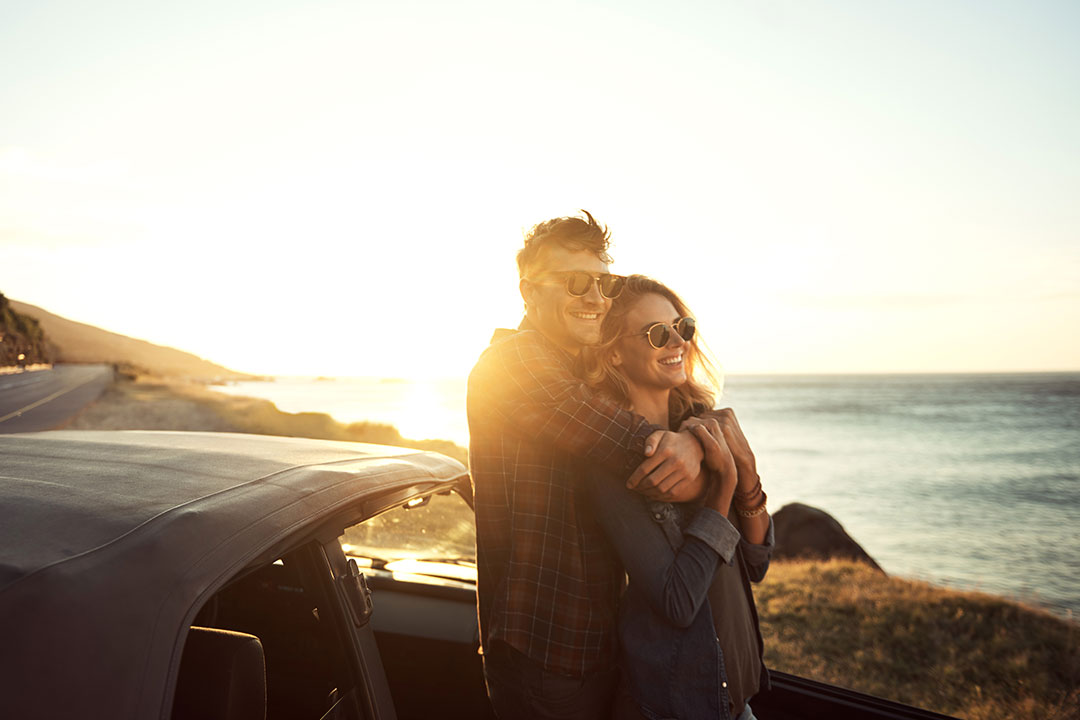 a happy couple standing outside of their car at sunset