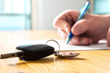 car keys resting on the table as a person signs a paper in the background